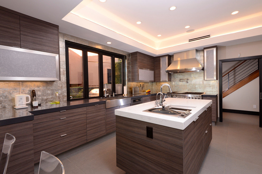 Photo of a large contemporary l-shaped open plan kitchen in Orange County with a farmhouse sink, flat-panel cabinets, dark wood cabinets, solid surface benchtops, metal splashback, stainless steel appliances, ceramic floors, with island, grey floor, metallic splashback, black benchtop and recessed.