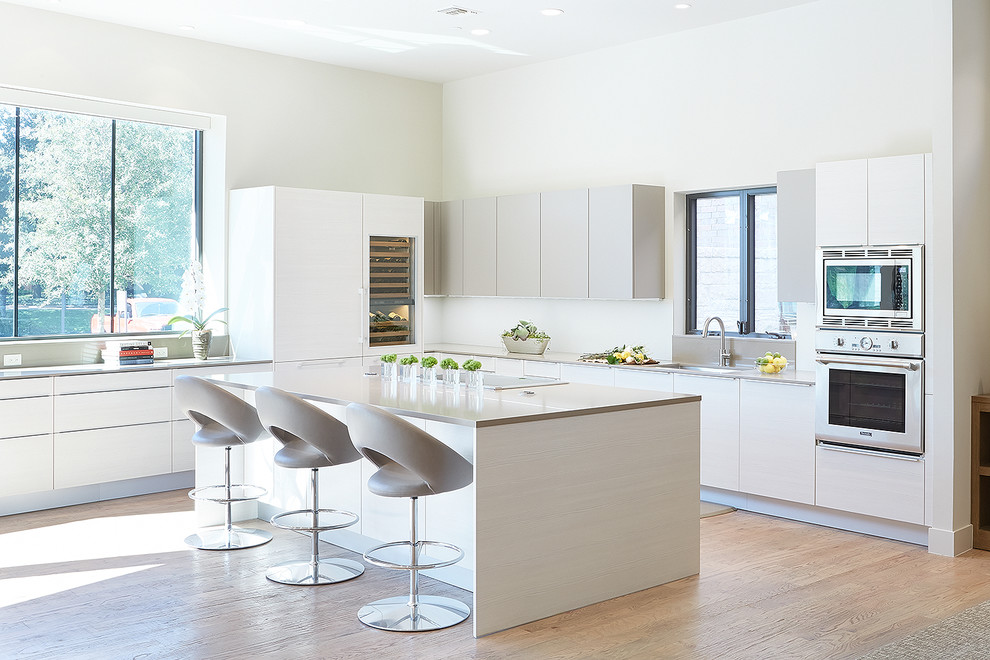 Photo of a contemporary l-shaped kitchen in Dallas with an undermount sink, flat-panel cabinets, white cabinets, stainless steel appliances, medium hardwood floors and with island.