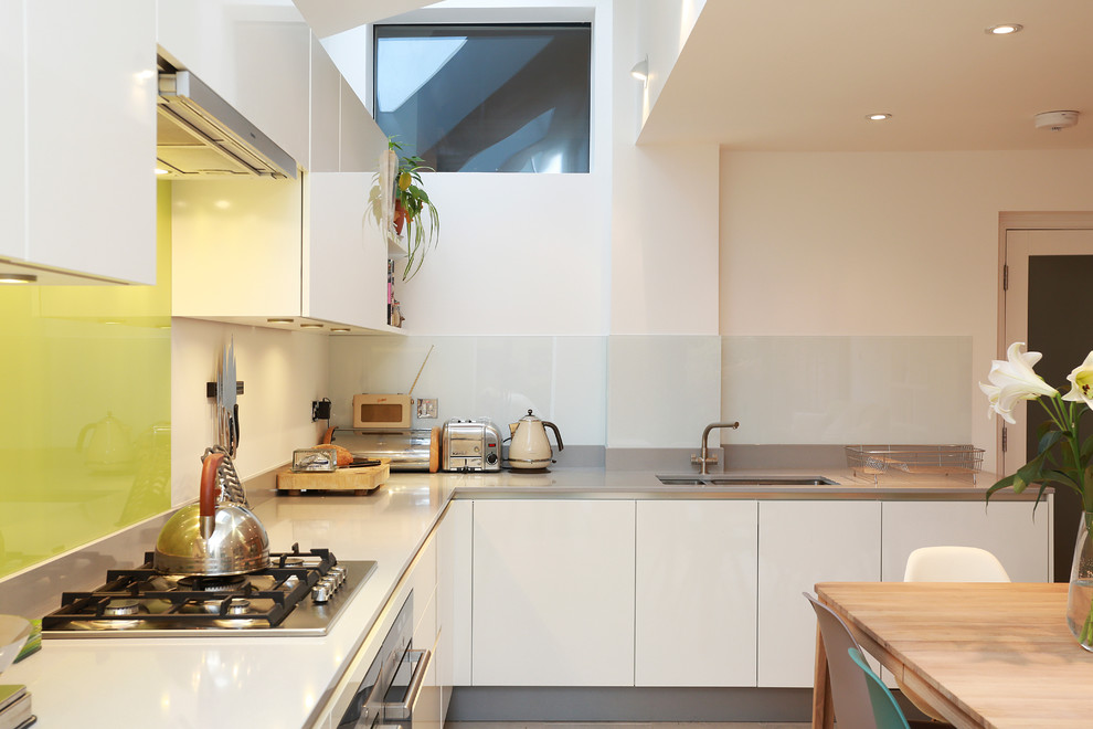 Photo of a large contemporary open plan kitchen in London with a drop-in sink, flat-panel cabinets, white cabinets, quartz benchtops, yellow splashback, glass sheet splashback, panelled appliances, no island and beige floor.