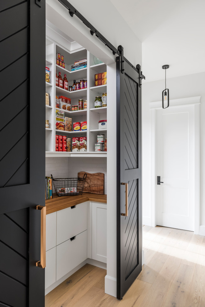 Example of a small kitchen pantry design with white cabinets, wood countertops, white backsplash and brown countertops