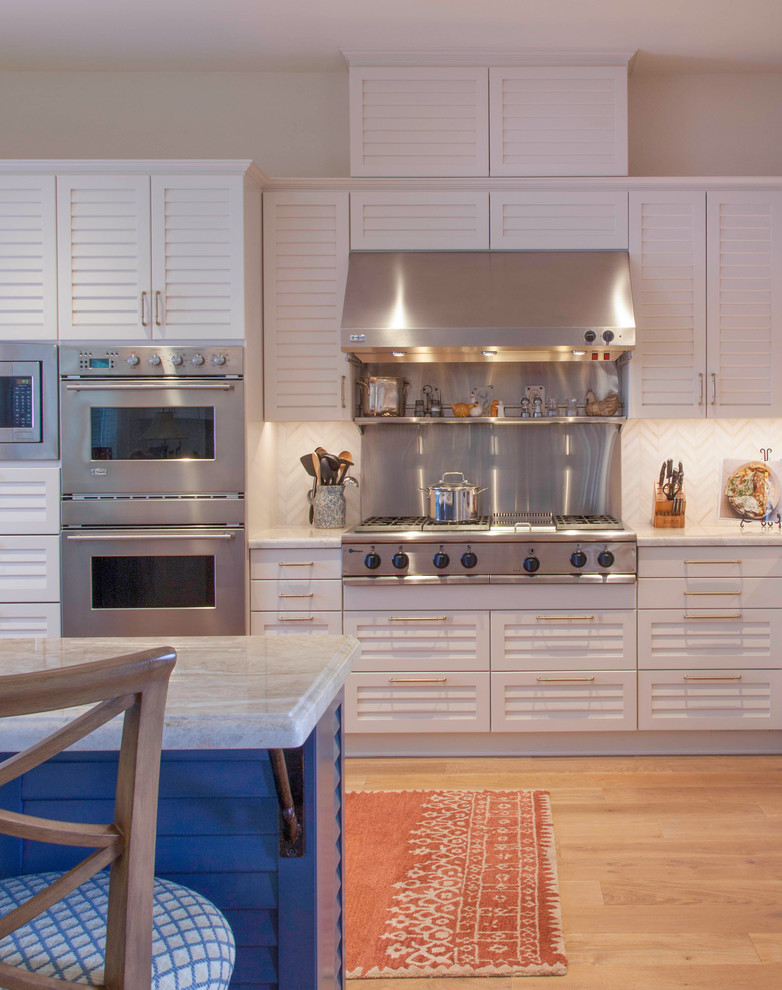 Design ideas for a mid-sized beach style single-wall eat-in kitchen in San Diego with louvered cabinets, white cabinets, marble benchtops, white splashback, ceramic splashback, stainless steel appliances, light hardwood floors, with island, brown floor and white benchtop.