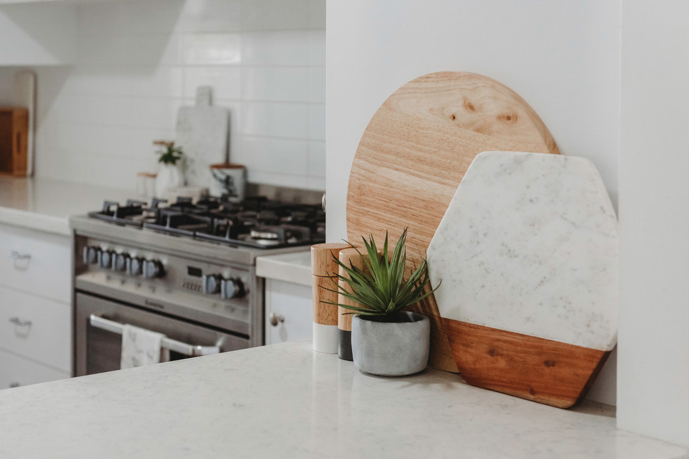 Mid-sized scandinavian u-shaped eat-in kitchen in Sunshine Coast with a double-bowl sink, open cabinets, white cabinets, marble benchtops, white splashback, subway tile splashback, white appliances, medium hardwood floors, with island and brown floor.