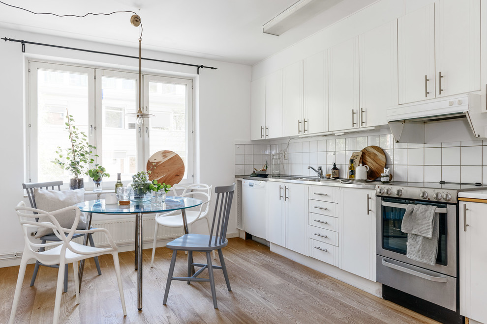 Design ideas for a mid-sized scandinavian single-wall eat-in kitchen in Stockholm with a double-bowl sink, white cabinets, white splashback, stainless steel appliances, light hardwood floors, no island and flat-panel cabinets.