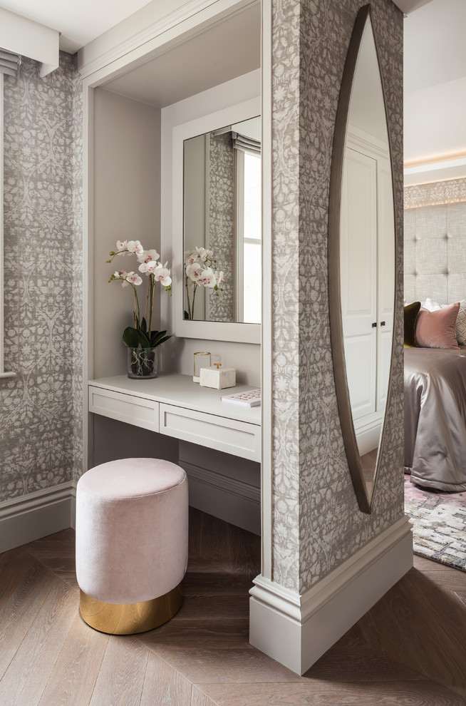 This is an example of a medium sized traditional wardrobe for women in London with recessed-panel cabinets, grey cabinets, medium hardwood flooring and brown floors.