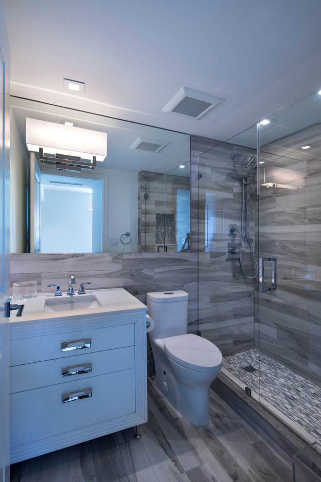 Inspiration for a small transitional 3/4 bathroom in Miami with furniture-like cabinets, white cabinets, gray tile, an undermount sink, solid surface benchtops, an alcove shower, a one-piece toilet, porcelain tile, white walls, porcelain floors, grey floor and a hinged shower door.