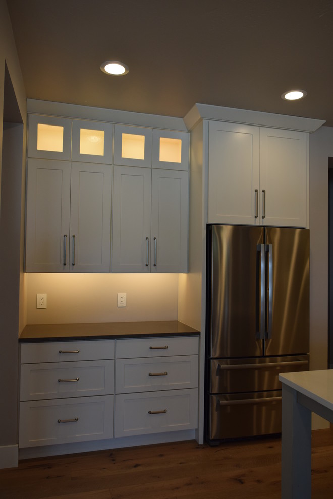 Transitional l-shaped medium tone wood floor open concept kitchen photo with a farmhouse sink, shaker cabinets, white cabinets, quartz countertops, gray backsplash, subway tile backsplash, stainless steel appliances and an island