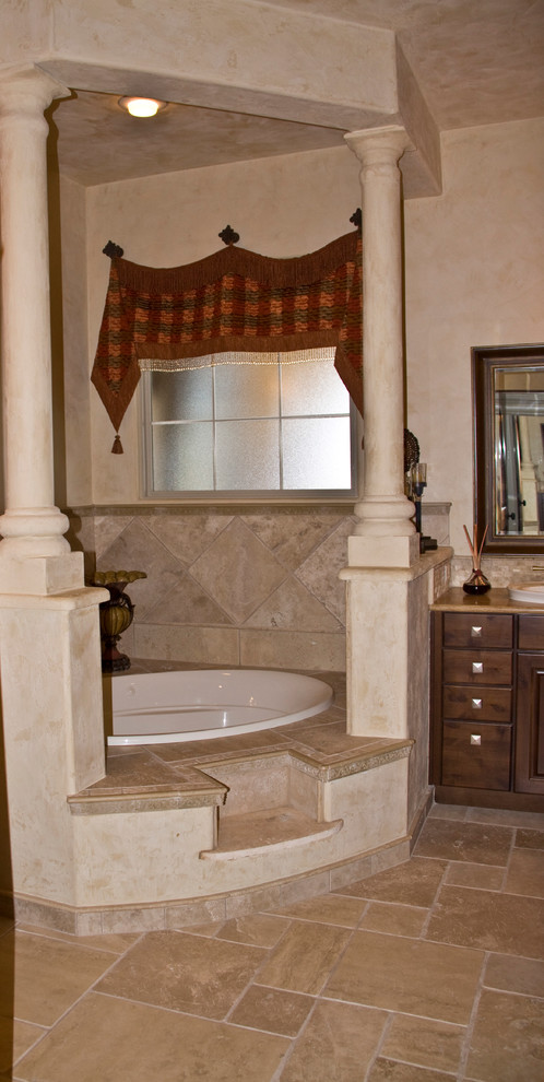 Inspiration for a mid-sized mediterranean master bathroom in Austin with a drop-in sink, raised-panel cabinets, medium wood cabinets, a drop-in tub, a two-piece toilet, beige tile, stone tile, beige walls and travertine floors.