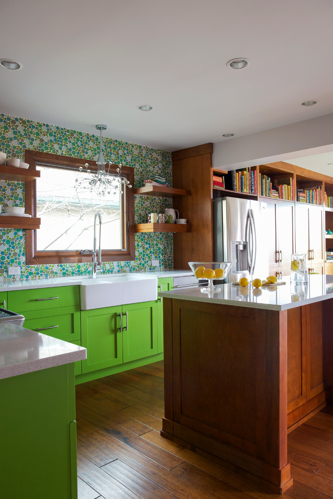 This is an example of a large eclectic l-shaped eat-in kitchen in Calgary with a farmhouse sink, shaker cabinets, green cabinets, quartz benchtops, green splashback, mosaic tile splashback, stainless steel appliances, light hardwood floors, multiple islands and beige floor.
