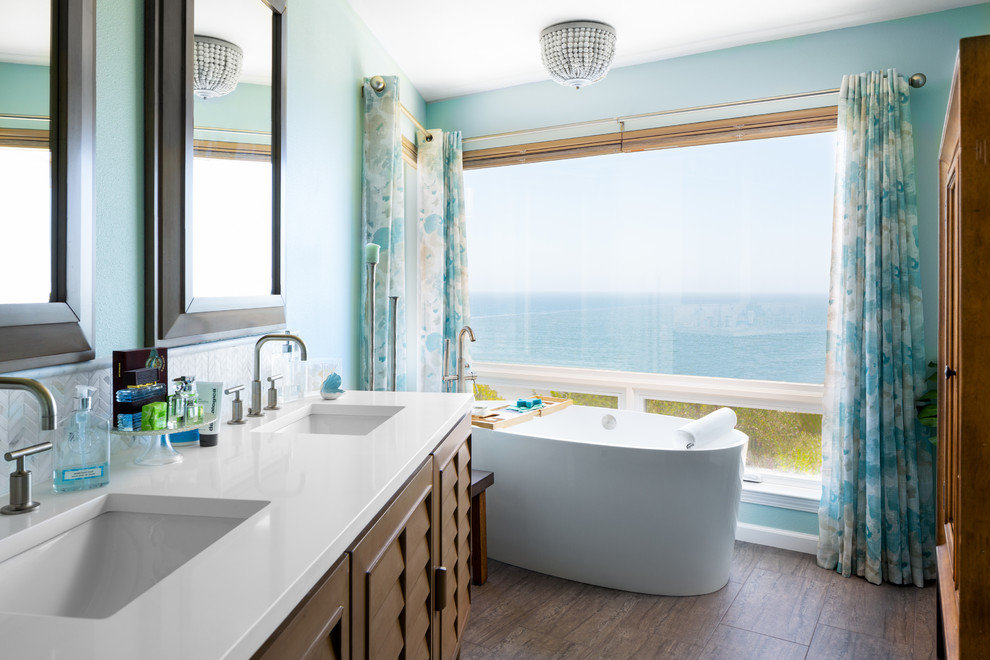 Design ideas for a mid-sized beach style master bathroom in San Francisco with louvered cabinets, medium wood cabinets, a freestanding tub, a curbless shower, a one-piece toilet, blue tile, ceramic tile, blue walls, porcelain floors, a drop-in sink, quartzite benchtops, brown floor, an open shower and white benchtops.