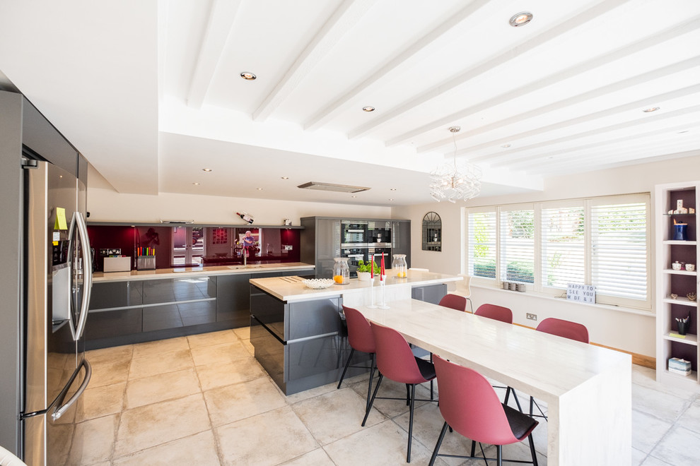 Large contemporary eat-in kitchen in Wiltshire with flat-panel cabinets, grey cabinets, solid surface benchtops, pink splashback, glass sheet splashback, with island, beige benchtop and beige floor.