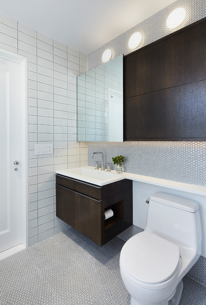 Mid-sized modern kids bathroom in New York with an integrated sink, flat-panel cabinets, dark wood cabinets, solid surface benchtops, an alcove tub, a one-piece toilet, blue tile, mosaic tile, blue walls and mosaic tile floors.