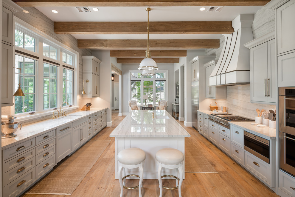 Inspiration for a mediterranean galley eat-in kitchen in Houston with an undermount sink, beaded inset cabinets, white cabinets, beige splashback, stainless steel appliances, medium hardwood floors, with island, brown floor and white benchtop.