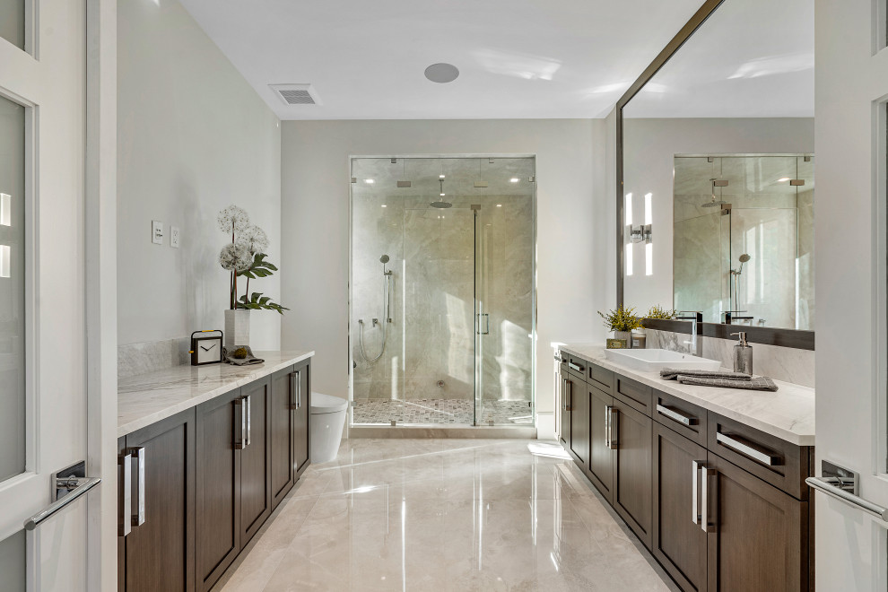 Example of a large transitional 3/4 stone slab marble floor, beige floor and single-sink alcove shower design in Miami with beaded inset cabinets, brown cabinets, a one-piece toilet, gray walls, a drop-in sink, marble countertops, a hinged shower door, white countertops and a built-in vanity