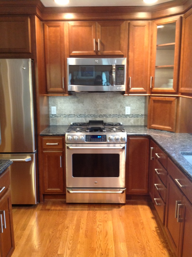 Example of a mid-sized transitional l-shaped medium tone wood floor eat-in kitchen design with an undermount sink, recessed-panel cabinets, medium tone wood cabinets, granite countertops, gray backsplash, stone tile backsplash, stainless steel appliances, gray walls and an island