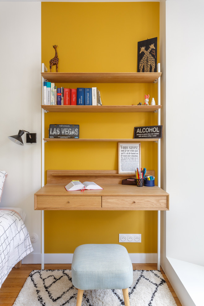 Bild på ett litet funkis hemmabibliotek, med gula väggar, ljust trägolv och ett fristående skrivbord