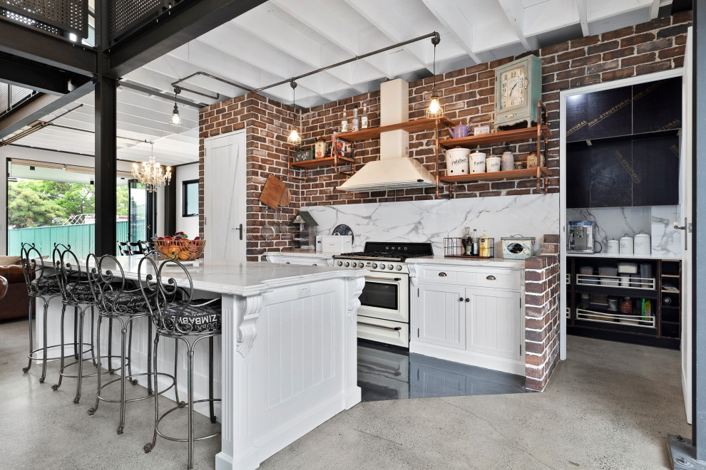 Mid-sized industrial galley open plan kitchen in Sydney with a farmhouse sink, shaker cabinets, white cabinets, marble benchtops, multi-coloured splashback, marble splashback, coloured appliances, concrete floors, with island, grey floor, multi-coloured benchtop and exposed beam.