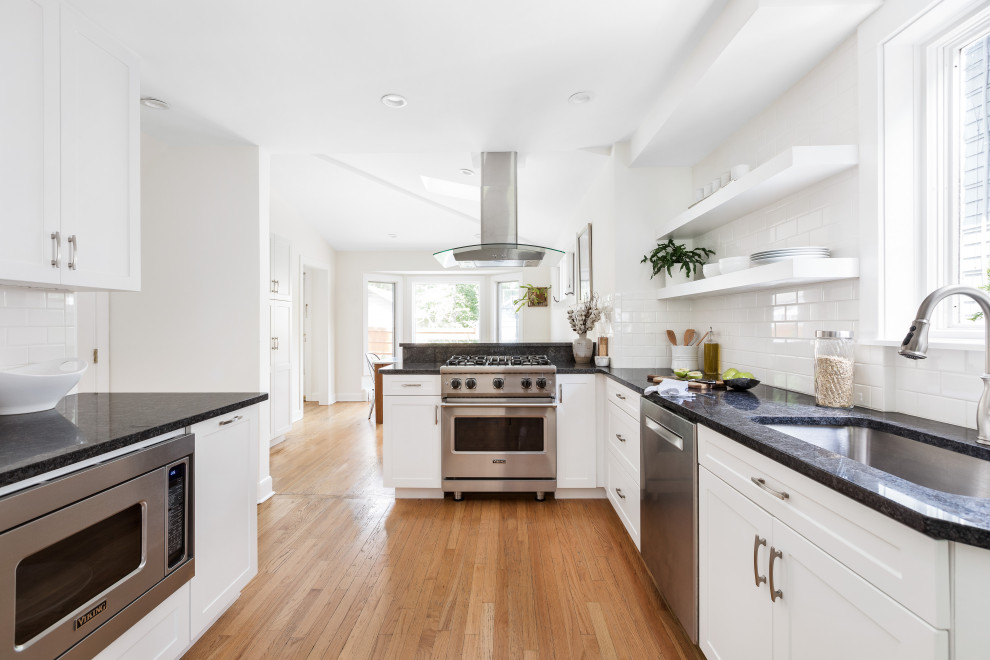 Eat-in kitchen - mid-sized transitional galley medium tone wood floor and brown floor eat-in kitchen idea in Philadelphia with a single-bowl sink, shaker cabinets, white cabinets, granite countertops, white backsplash, ceramic backsplash, stainless steel appliances and black countertops