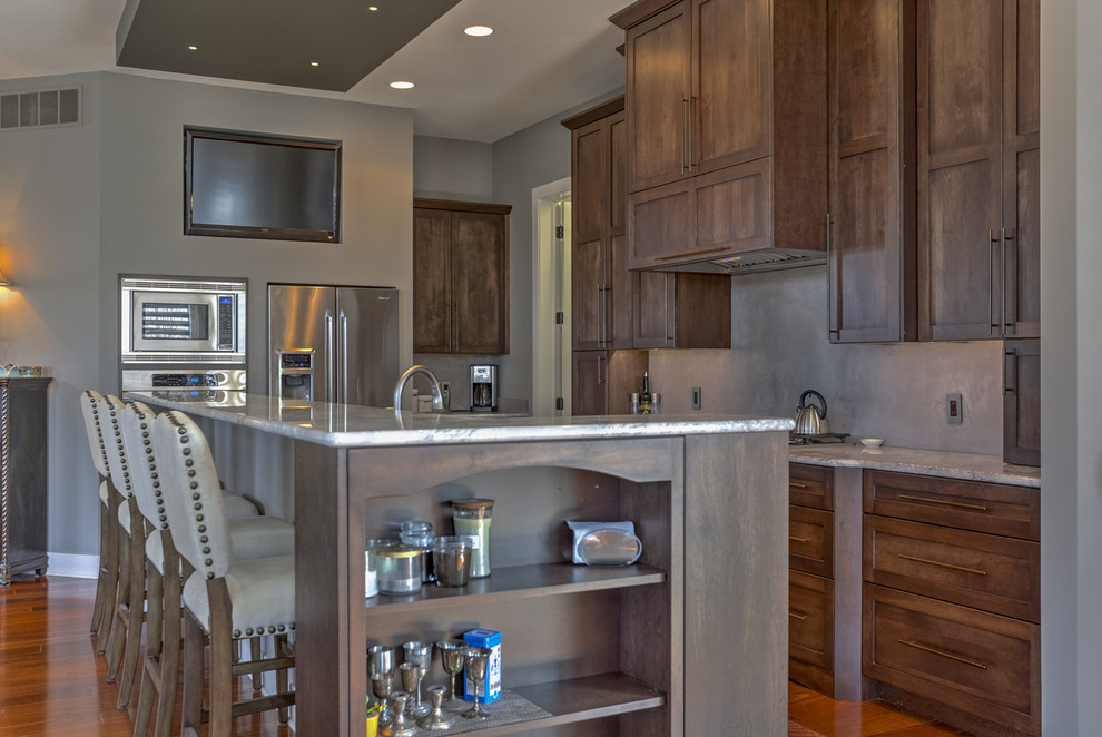 Medium tone wood floor eat-in kitchen photo with dark wood cabinets, granite countertops, gray backsplash, stainless steel appliances and an island