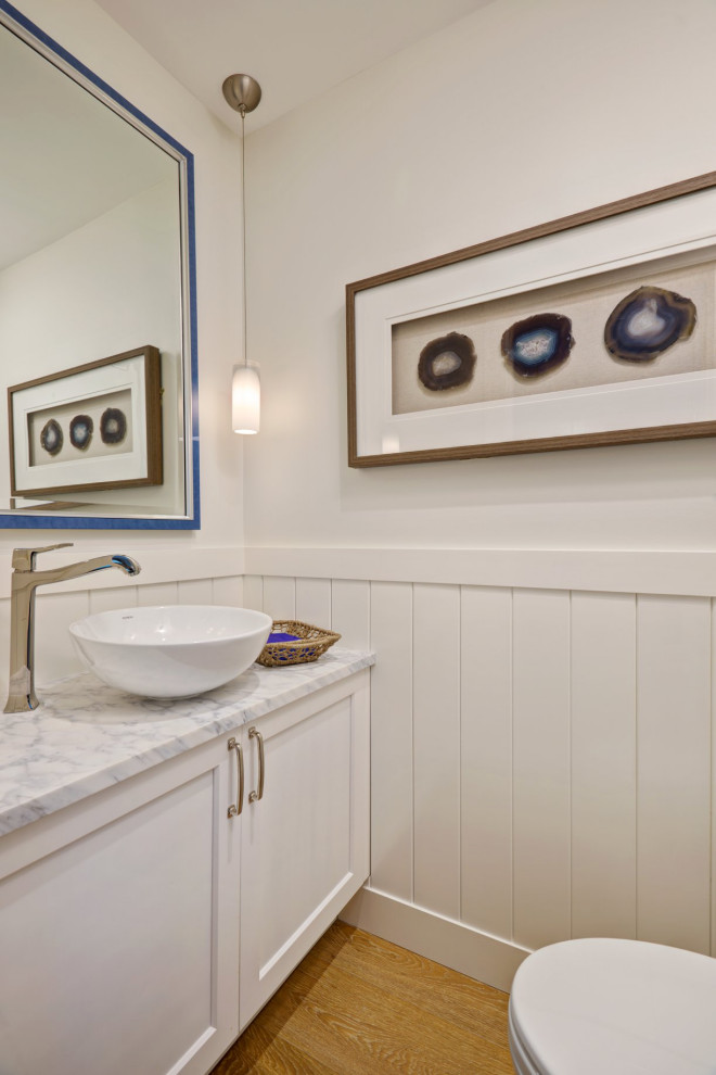 Inspiration for a small beach style powder room with shaker cabinets, white cabinets, a one-piece toilet, white walls, medium hardwood floors, a vessel sink, marble benchtops, a built-in vanity and planked wall panelling.