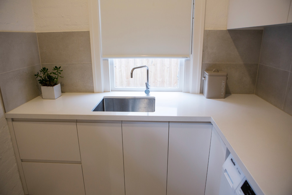 Photo of a small contemporary l-shaped dedicated laundry room in Melbourne with an undermount sink, white cabinets, quartz benchtops, a side-by-side washer and dryer, flat-panel cabinets and white walls.