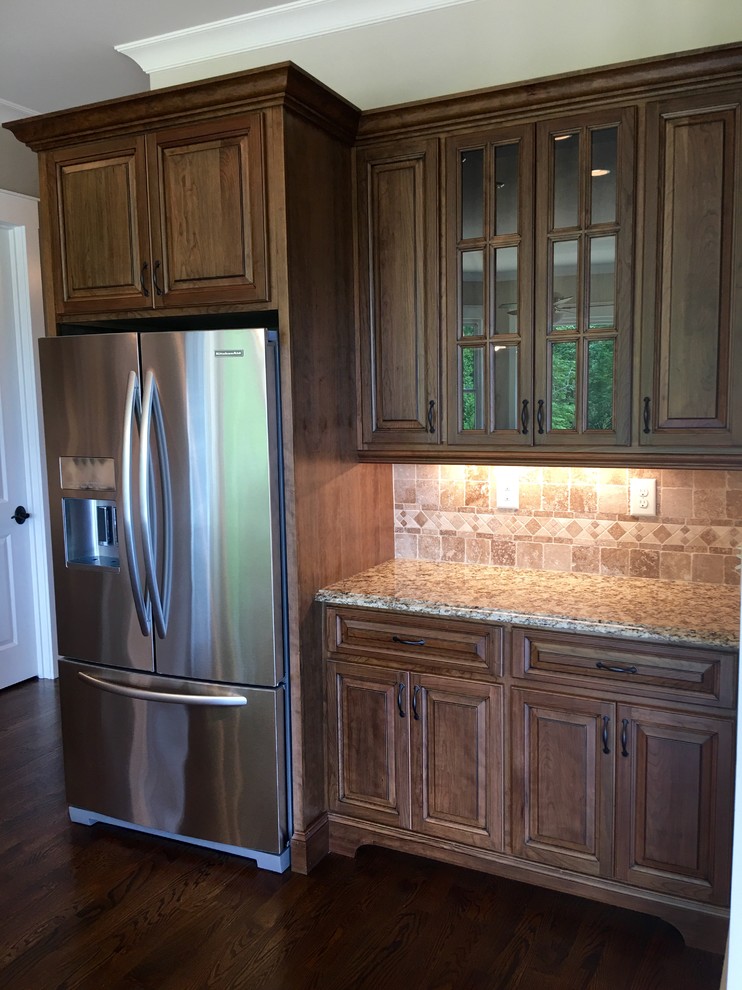 Photo of a large transitional l-shaped kitchen in Atlanta with an undermount sink, raised-panel cabinets, medium wood cabinets, granite benchtops, beige splashback, mosaic tile splashback, stainless steel appliances, dark hardwood floors and with island.