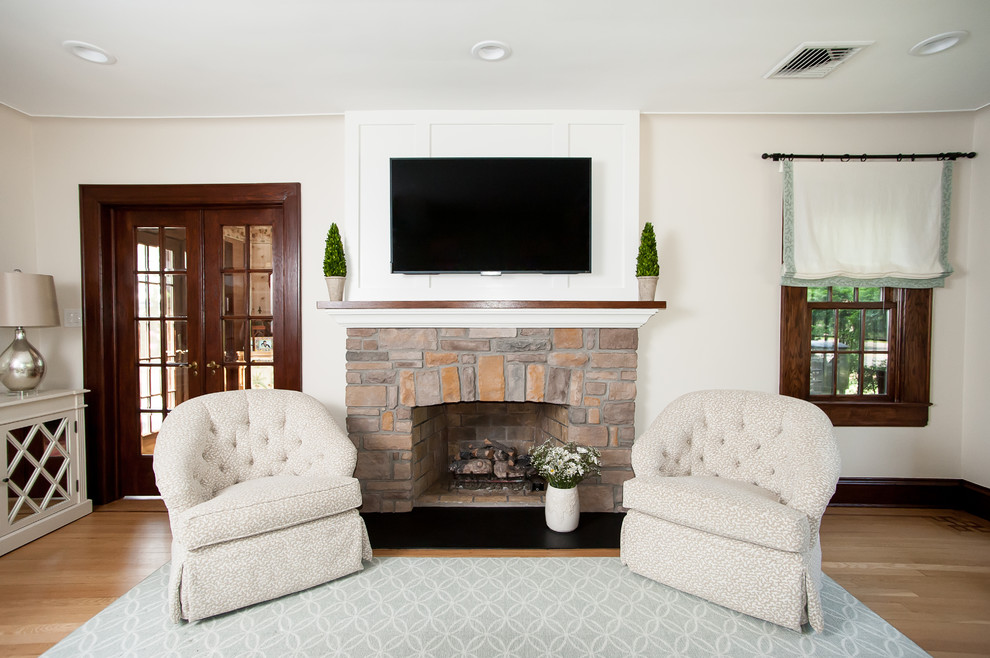 This is an example of a traditional living room in New York with white walls, light hardwood floors, a stone fireplace surround and a wall-mounted tv.