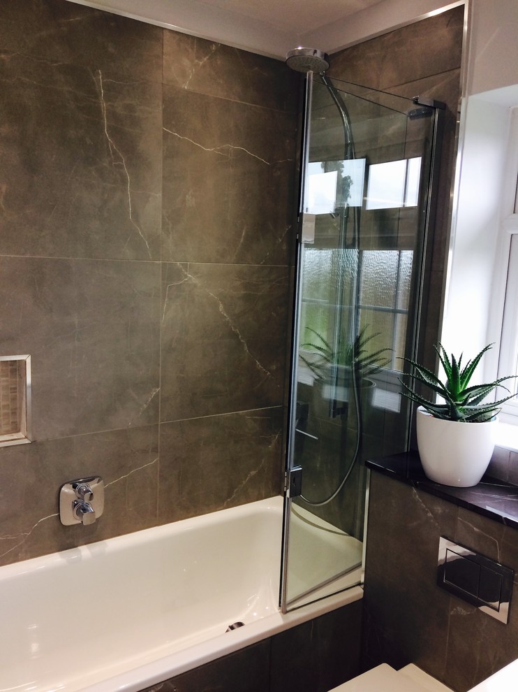 Small contemporary kids bathroom in Surrey with a drop-in tub, a shower/bathtub combo, a wall-mount toilet, gray tile, porcelain tile, porcelain floors, marble benchtops and a hinged shower door.