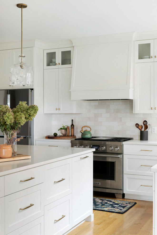 Foto di una cucina chic con ante bianche, paraspruzzi beige, elettrodomestici in acciaio inossidabile e pavimento in legno massello medio
