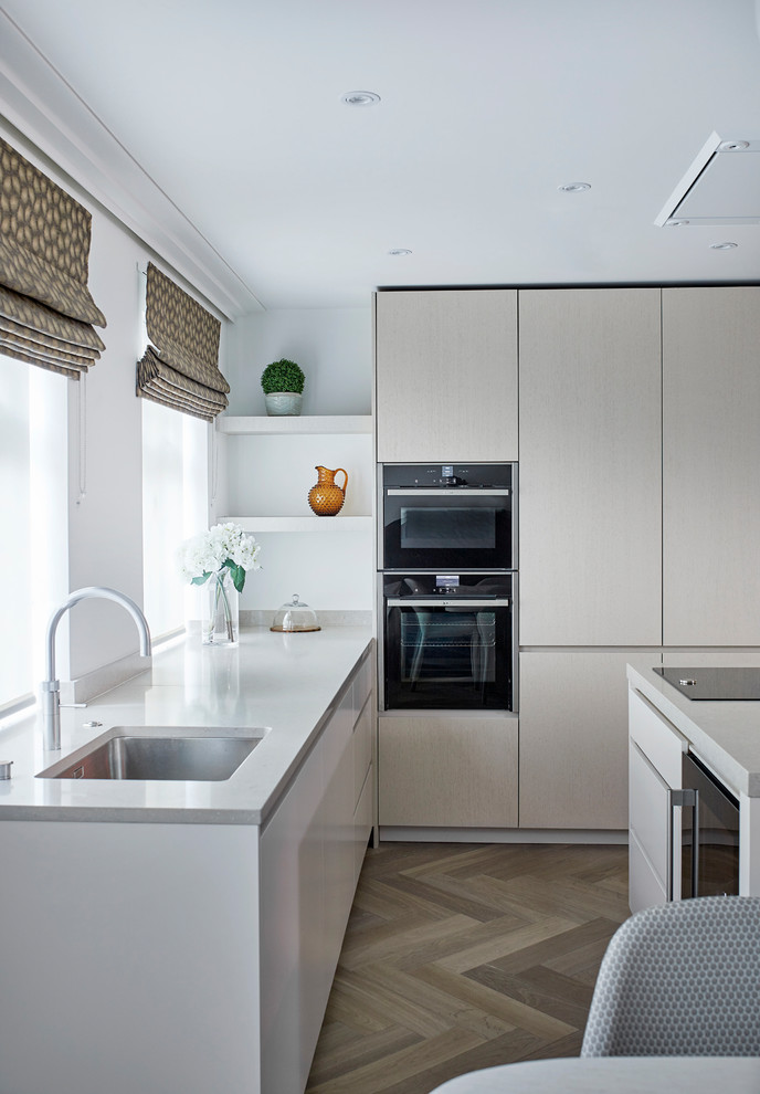 Photo of a large modern l-shaped eat-in kitchen in London with an integrated sink, recessed-panel cabinets, light wood cabinets, solid surface benchtops, beige splashback, marble splashback, panelled appliances, medium hardwood floors and with island.