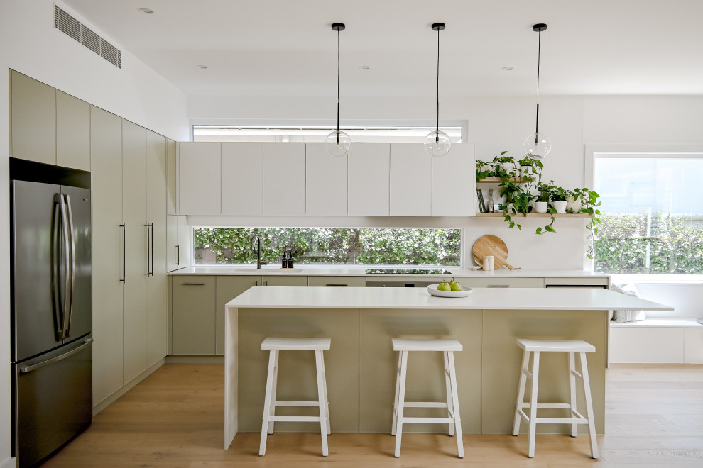 This is an example of a mid-sized tropical galley open plan kitchen in Sydney with a drop-in sink, shaker cabinets, green cabinets, quartz benchtops, multi-coloured splashback, window splashback, stainless steel appliances, light hardwood floors, with island, brown floor and white benchtop.