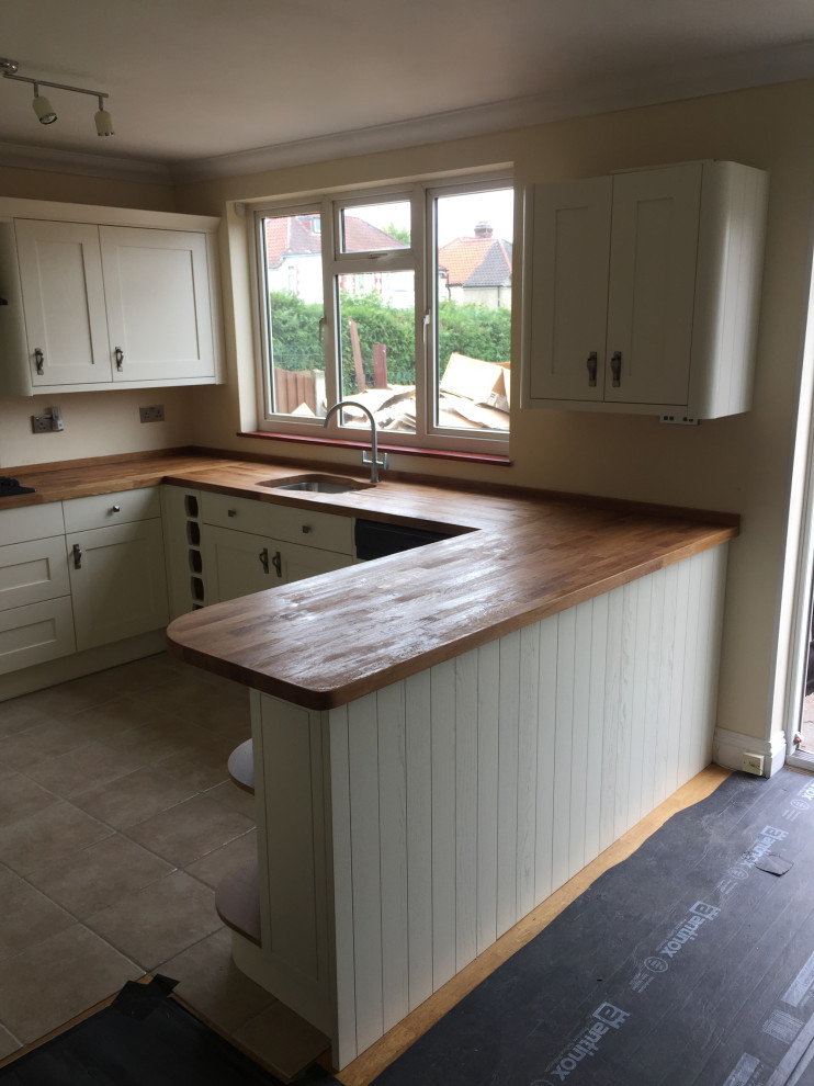 Photo of a large traditional u-shaped open plan kitchen in London with an integrated sink, shaker cabinets, white cabinets, wood benchtops, panelled appliances, ceramic floors, grey floor and multi-coloured benchtop.