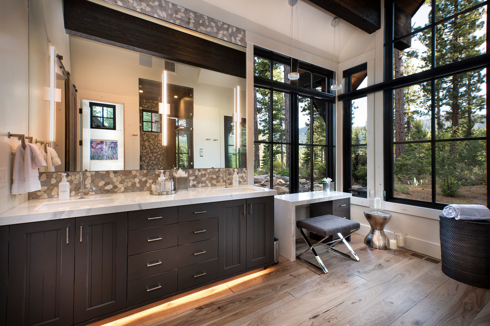 Large mountain style master multicolored tile and pebble tile medium tone wood floor and brown floor bathroom photo with recessed-panel cabinets, dark wood cabinets, white walls, an undermount sink, white countertops and marble countertops