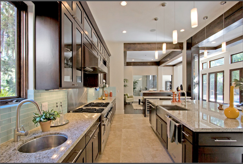 Photo of a large contemporary l-shaped open plan kitchen in Los Angeles with a farmhouse sink, shaker cabinets, dark wood cabinets, quartzite benchtops, blue splashback, glass tile splashback, stainless steel appliances, travertine floors and with island.
