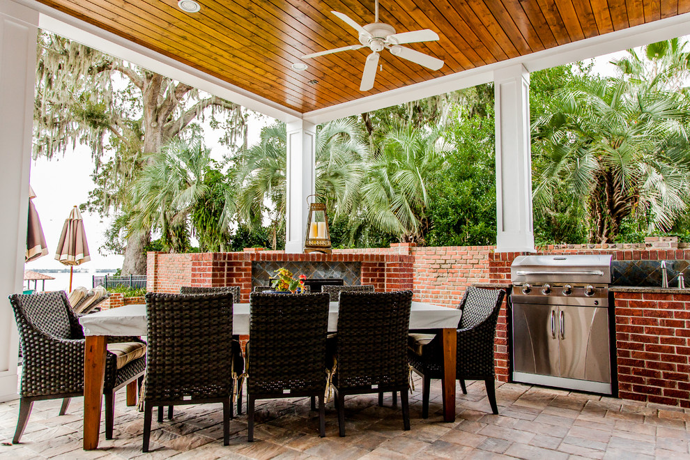 This is an example of a large traditional backyard verandah in Jacksonville with an outdoor kitchen, natural stone pavers and a roof extension.