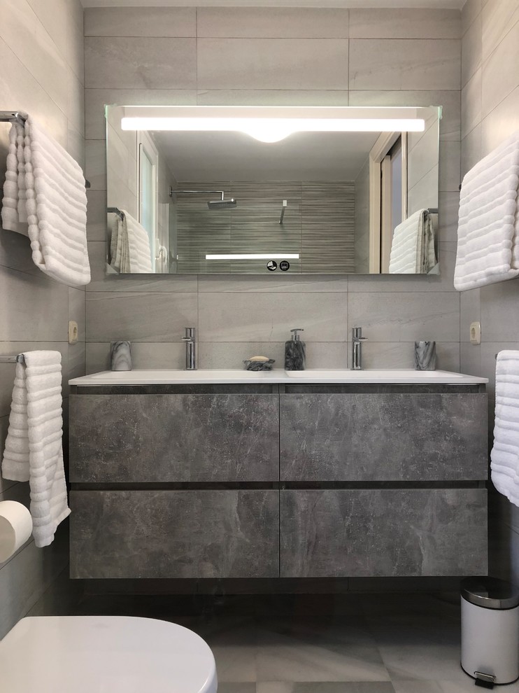 This is an example of a mid-sized eclectic 3/4 bathroom in Other with recessed-panel cabinets, white cabinets, a curbless shower, a two-piece toilet, gray tile, ceramic tile, grey walls, marble floors, an integrated sink, white floor and white benchtops.