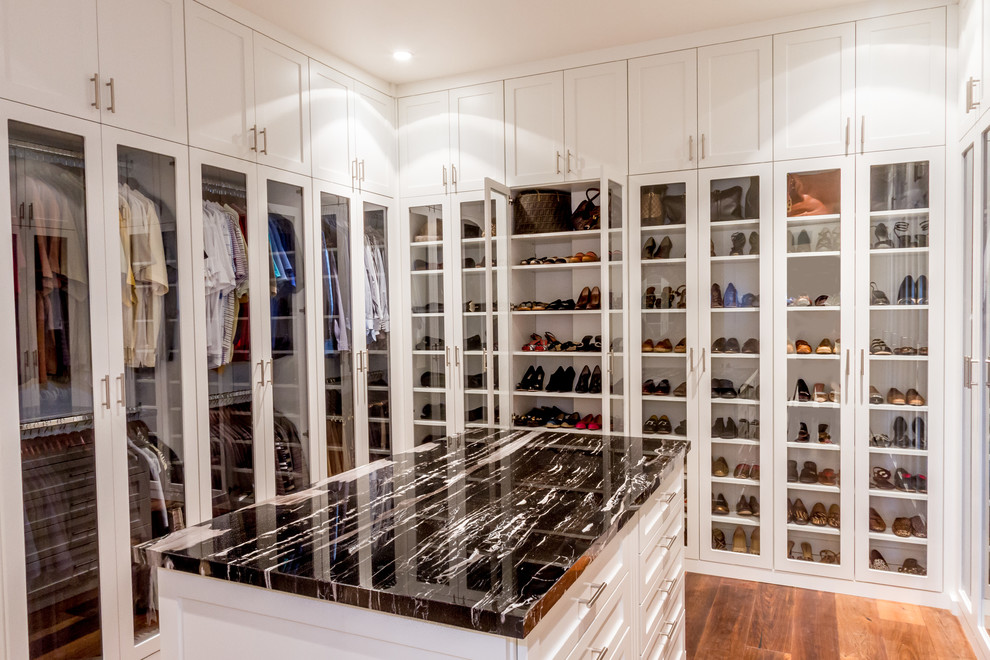 This is an example of a contemporary gender-neutral walk-in wardrobe in Minneapolis with glass-front cabinets, white cabinets, medium hardwood floors and brown floor.