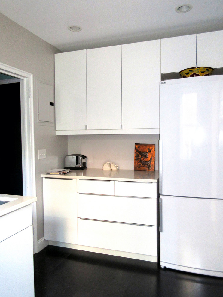 Photo of a small modern galley separate kitchen in New York with a drop-in sink, flat-panel cabinets, white cabinets, quartz benchtops, white splashback, subway tile splashback, white appliances, vinyl floors, no island and black floor.