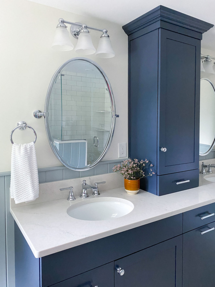 На фото: главная ванная комната в стиле кантри с фасадами в стиле шейкер, синими фасадами, отдельно стоящей ванной, угловым душем, раздельным унитазом, белой плиткой, керамической плиткой, белыми стенами, полом из керамогранита, врезной раковиной, столешницей из искусственного кварца, бежевым полом, душем с распашными дверями, бежевой столешницей, сиденьем для душа, тумбой под две раковины и встроенной тумбой