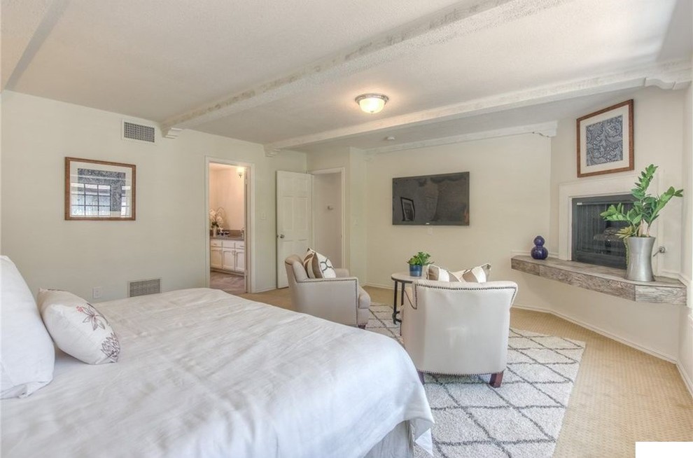 Photo of a mid-sized modern master bedroom in Los Angeles with white walls, carpet, a wood stove, a plaster fireplace surround and beige floor.