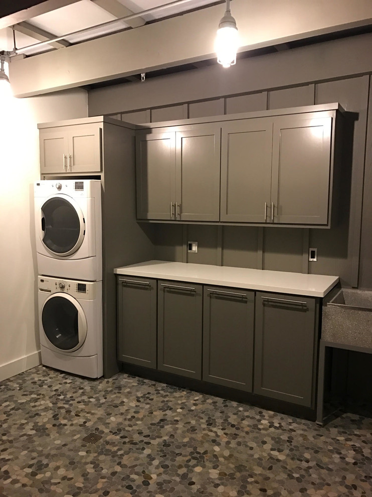 Photo of a large contemporary single-wall utility room in Santa Barbara with an utility sink, shaker cabinets, grey cabinets, quartz benchtops, grey walls, a stacked washer and dryer and grey floor.