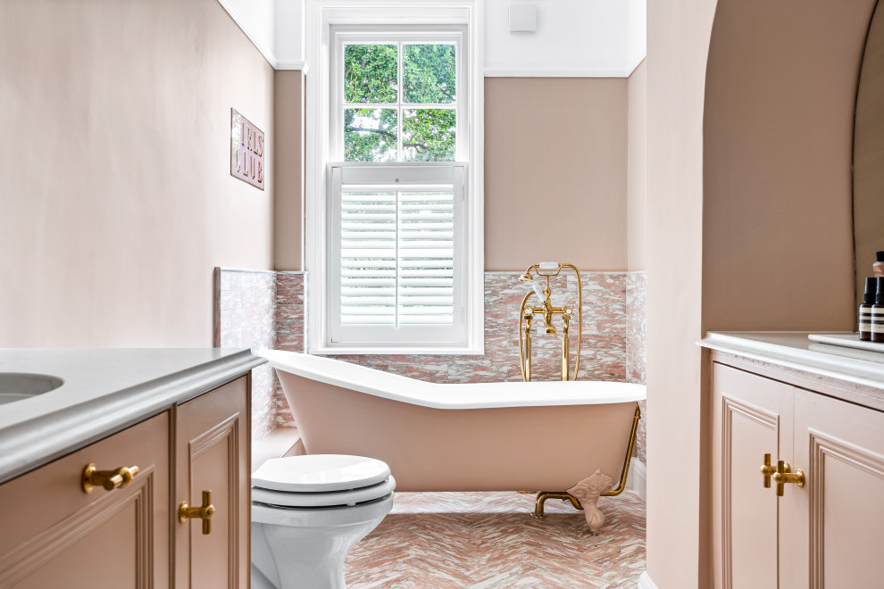 Photo of a traditional bathroom in Hertfordshire with recessed-panel cabinets, a claw-foot tub, pink tile, pink walls, an undermount sink, pink floor, white benchtops and a built-in vanity.