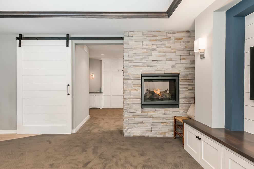 Inspiration for a large transitional look-out basement in Minneapolis with grey walls, carpet, a two-sided fireplace, a stone fireplace surround and grey floor.