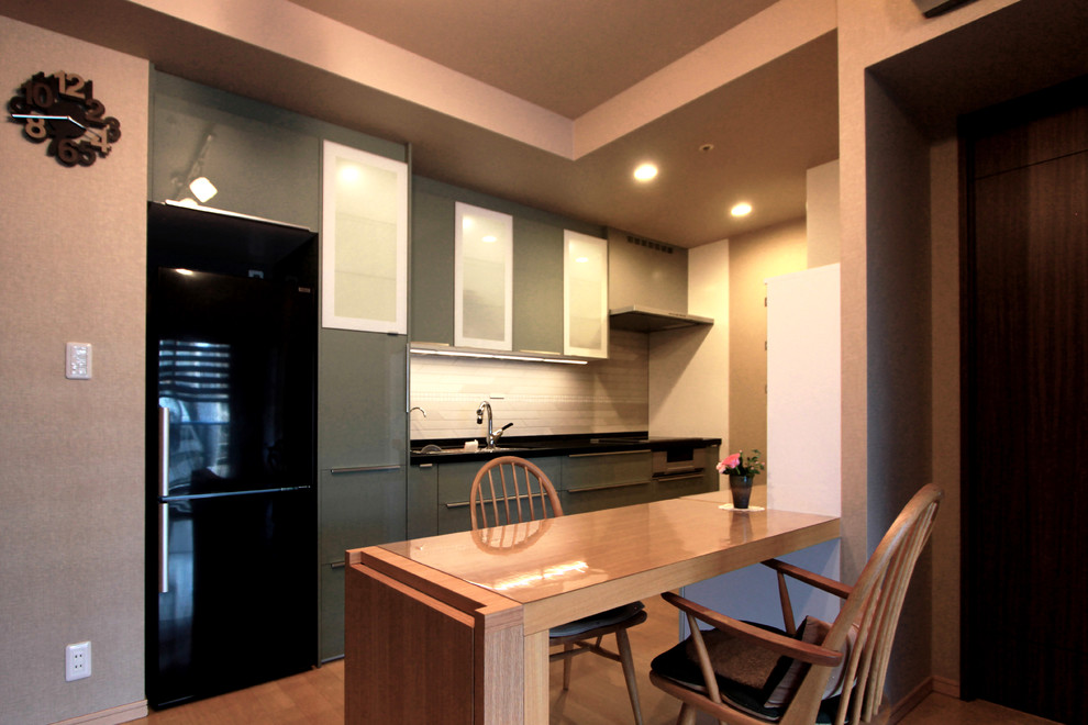 Mid-sized modern galley open plan kitchen in Tokyo with an undermount sink, flat-panel cabinets, green cabinets, solid surface benchtops, beige splashback, matchstick tile splashback, black appliances, plywood floors and black benchtop.