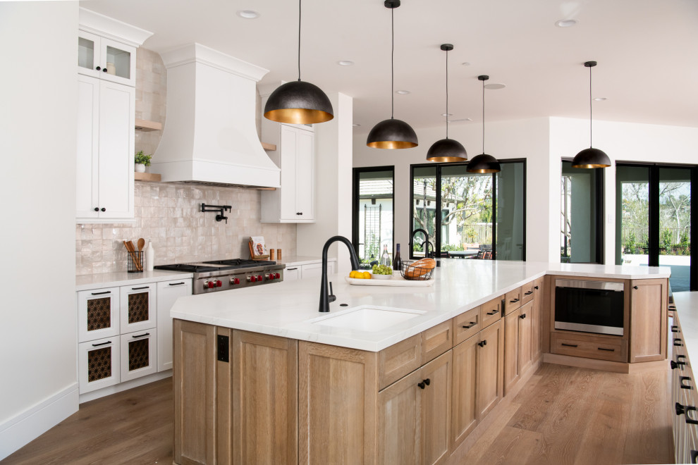 Inspiration for a transitional vinyl floor and brown floor enclosed kitchen remodel in Orange County with a farmhouse sink, shaker cabinets, white cabinets, quartz countertops, beige backsplash, terra-cotta backsplash, stainless steel appliances, an island and white countertops