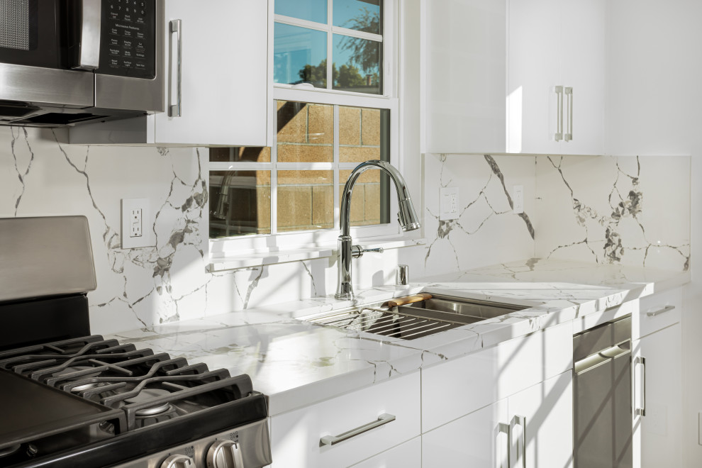 Small traditional single-wall open plan kitchen in Los Angeles with an undermount sink, flat-panel cabinets, white cabinets, quartz benchtops, white splashback, engineered quartz splashback, stainless steel appliances, laminate floors, no island, brown floor, white benchtop and vaulted.