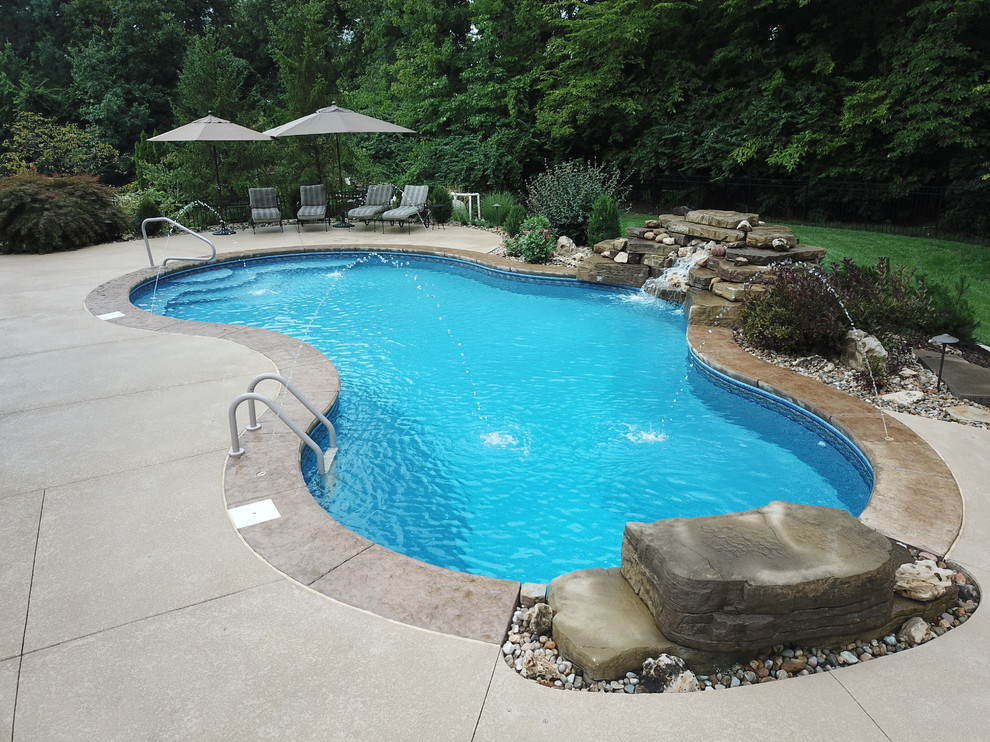 Design ideas for a mid-sized traditional backyard custom-shaped natural pool in St Louis with a water feature and stamped concrete.