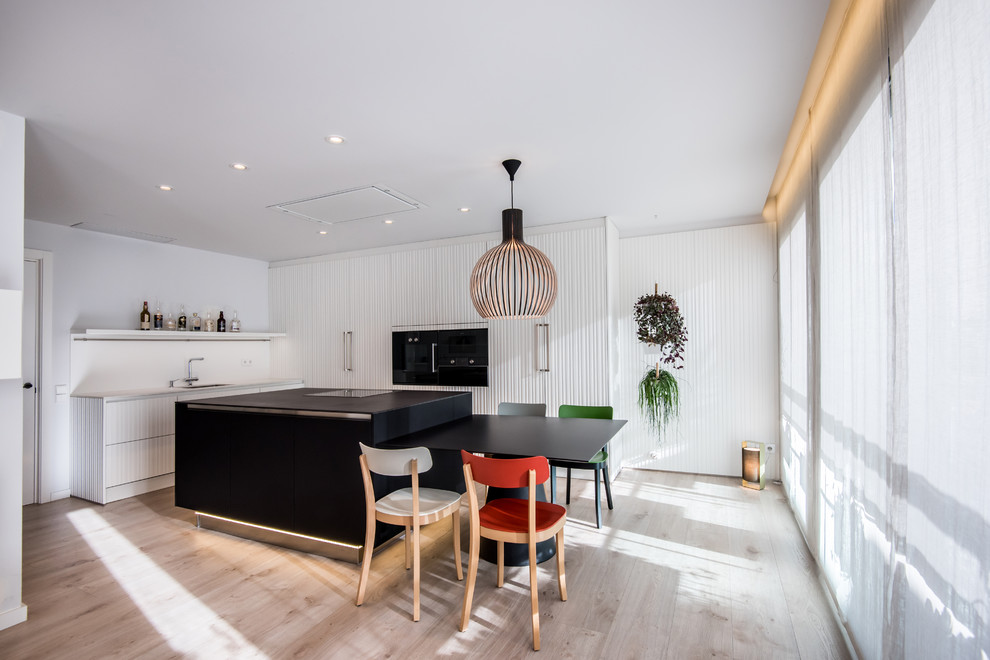 Design ideas for a mid-sized contemporary eat-in kitchen in Barcelona with a double-bowl sink, white cabinets, white splashback, black appliances, with island and brown floor.