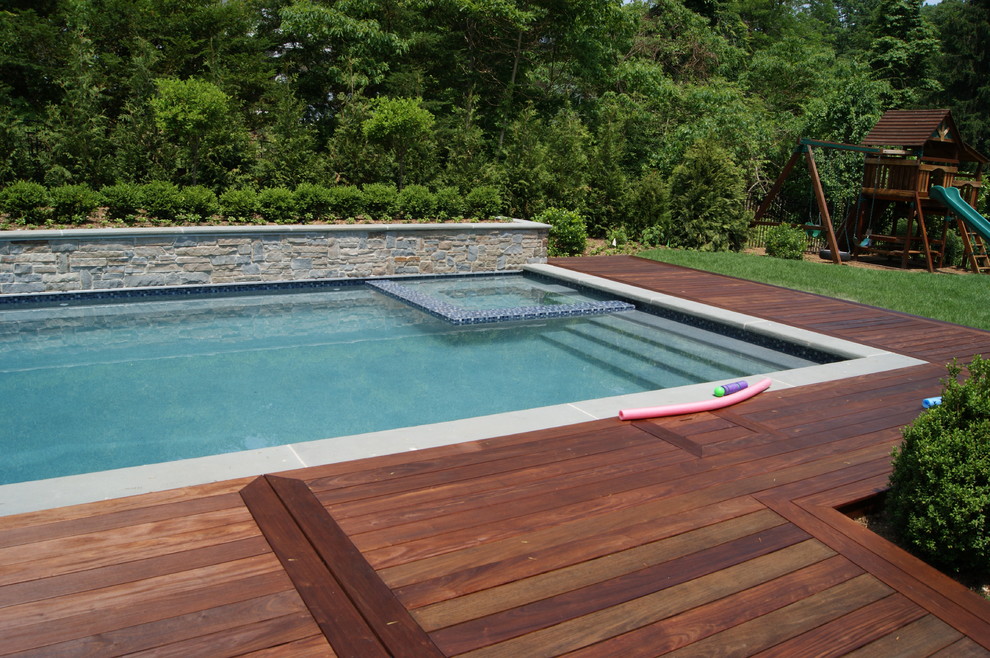This is an example of an expansive contemporary backyard lap pool in New York with a hot tub and decking.