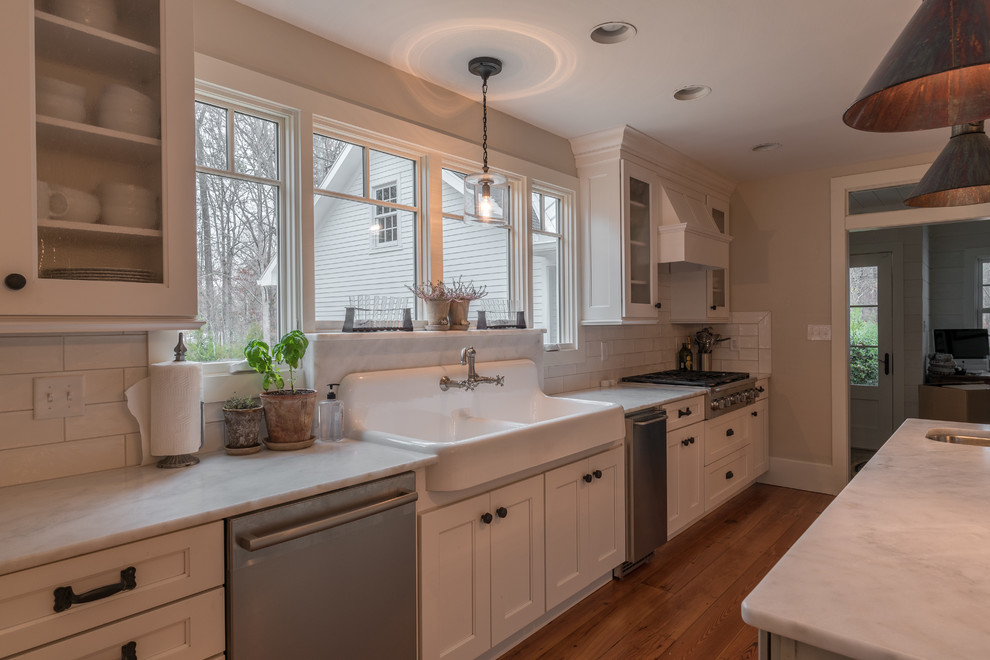 Kitchen - mid-sized transitional medium tone wood floor kitchen idea with a farmhouse sink, recessed-panel cabinets, white cabinets, marble countertops, white backsplash, subway tile backsplash, stainless steel appliances and an island