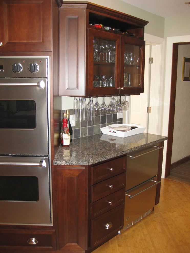 This is an example of a traditional galley eat-in kitchen in Boston with an undermount sink, shaker cabinets, dark wood cabinets, granite benchtops, grey splashback, ceramic splashback, stainless steel appliances, light hardwood floors, a peninsula and black benchtop.